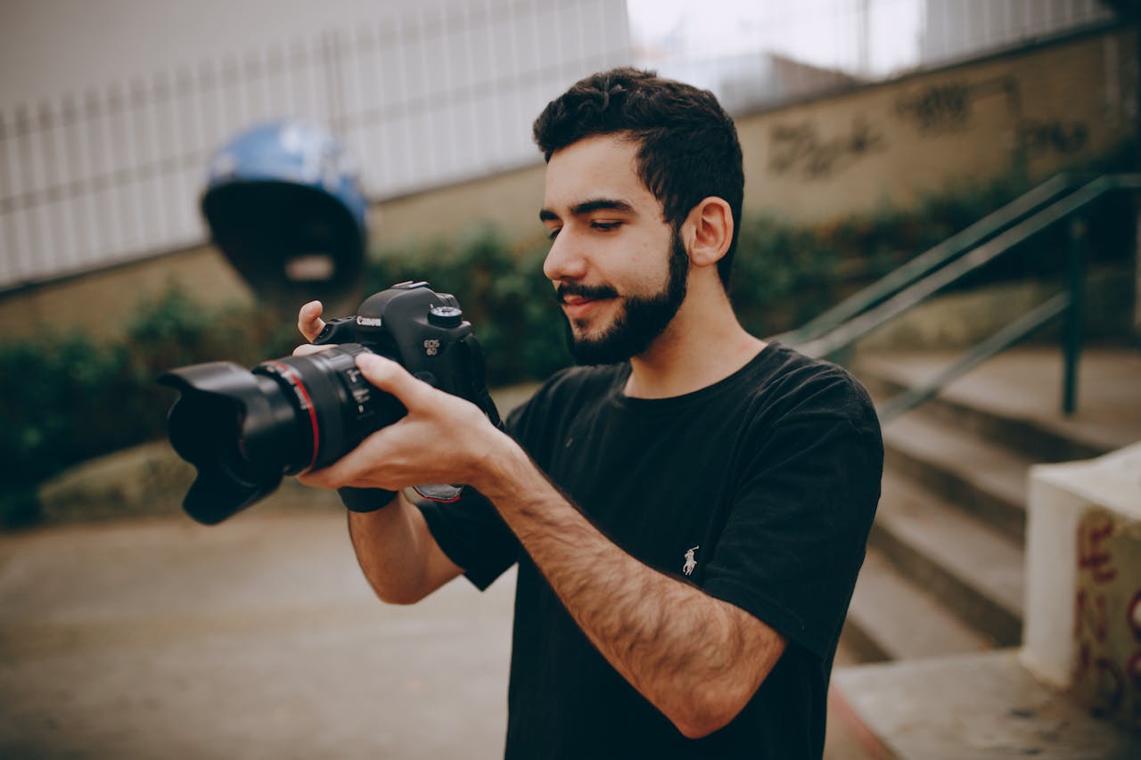 A young man focusing a DSLR camera outdoors, preparing for a photoshoot.
